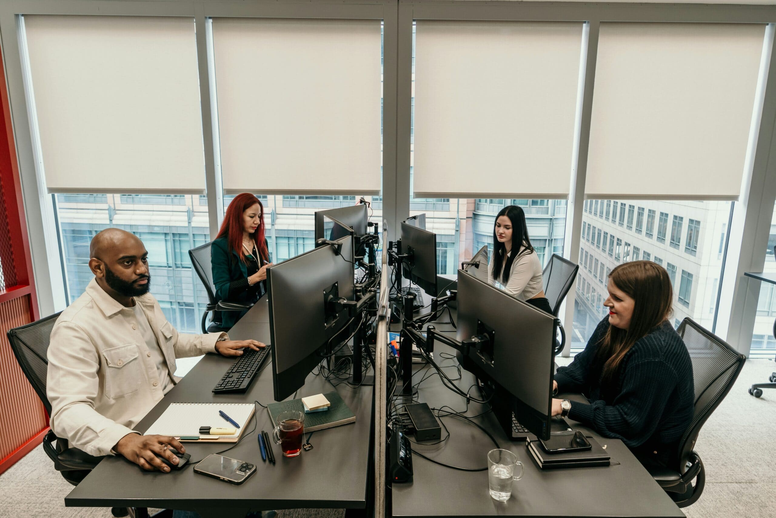 Four IT consultants work on computers at desks in a modern office, focusing intently on their screens.